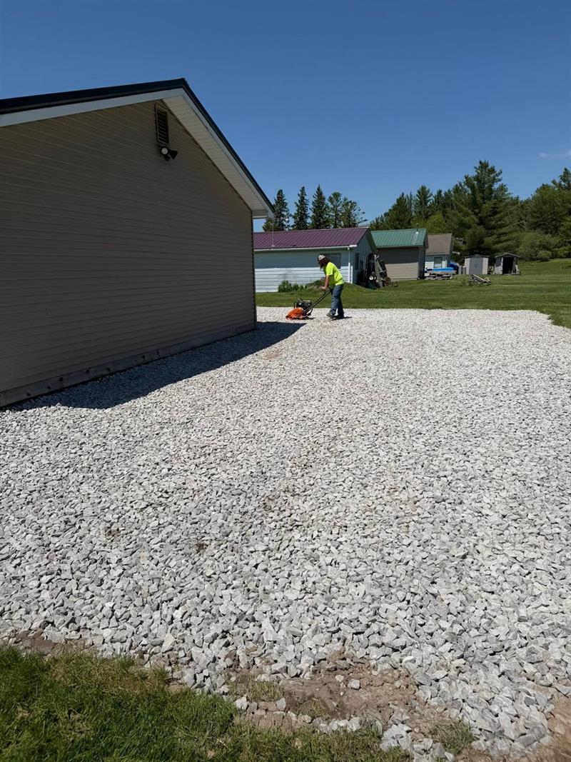 Plate-compacting a new gravel parking pad by a pole barn