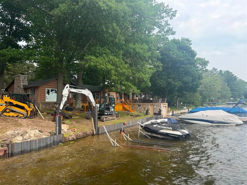 Track loader and mini excavator installing steel seawall panels at a lakefront