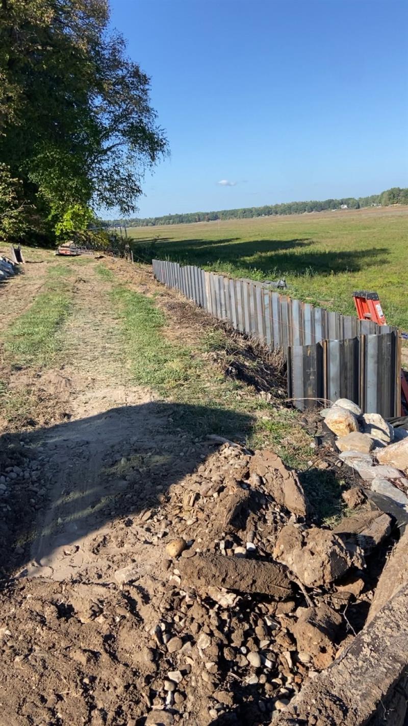 New steel sheet piling running along a graded shoreline bank