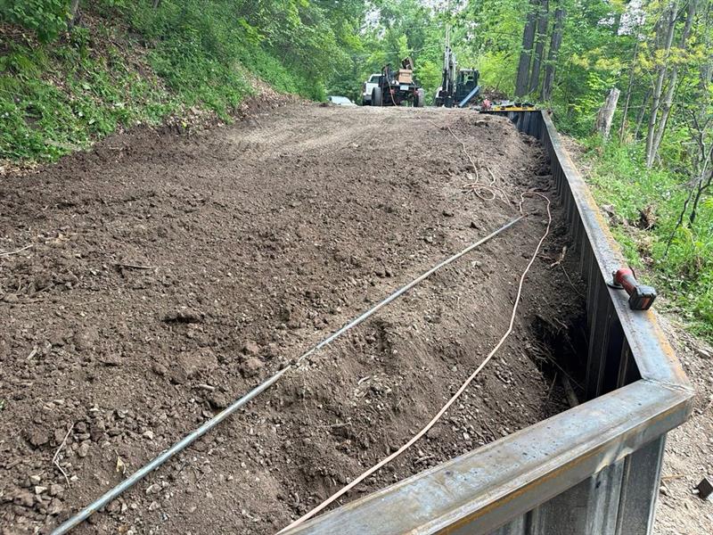 Graded backfill behind a new steel wall on a wooded bank