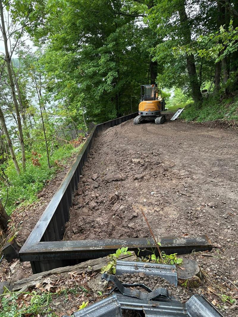 Mini excavator grading backfill behind a new steel seawall above the lake