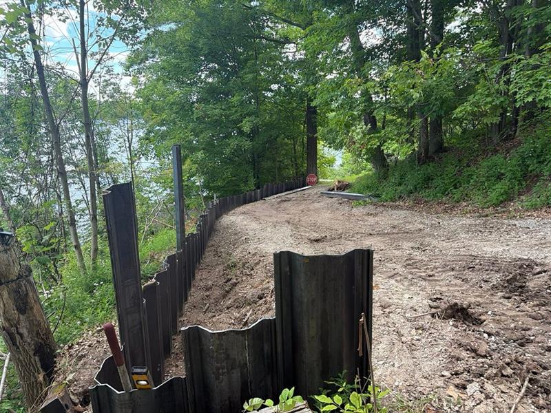 Curved run of steel sheet piling along a graded lakeside bank