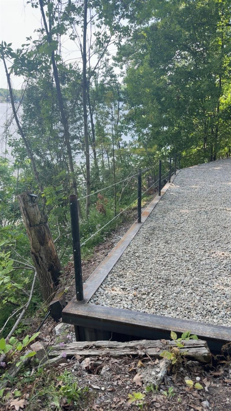 Finished gravel pad edged by a new steel wall with cable rail above the lake